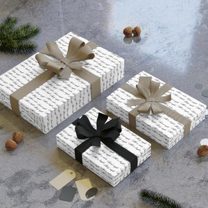 May include: Three wrapped gift boxes with white paper covered in script, tied with ribbons. Two boxes have tan ribbons and bows, while the third has a black ribbon and bow. The gifts are on a gray surface.