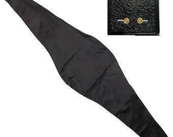 May include: A long, black, tapered fabric strap with a smooth texture. The inset shows a square, black, textured panel featuring two gold-colored circular metal studs positioned horizontally near the bottom edge of the panel.