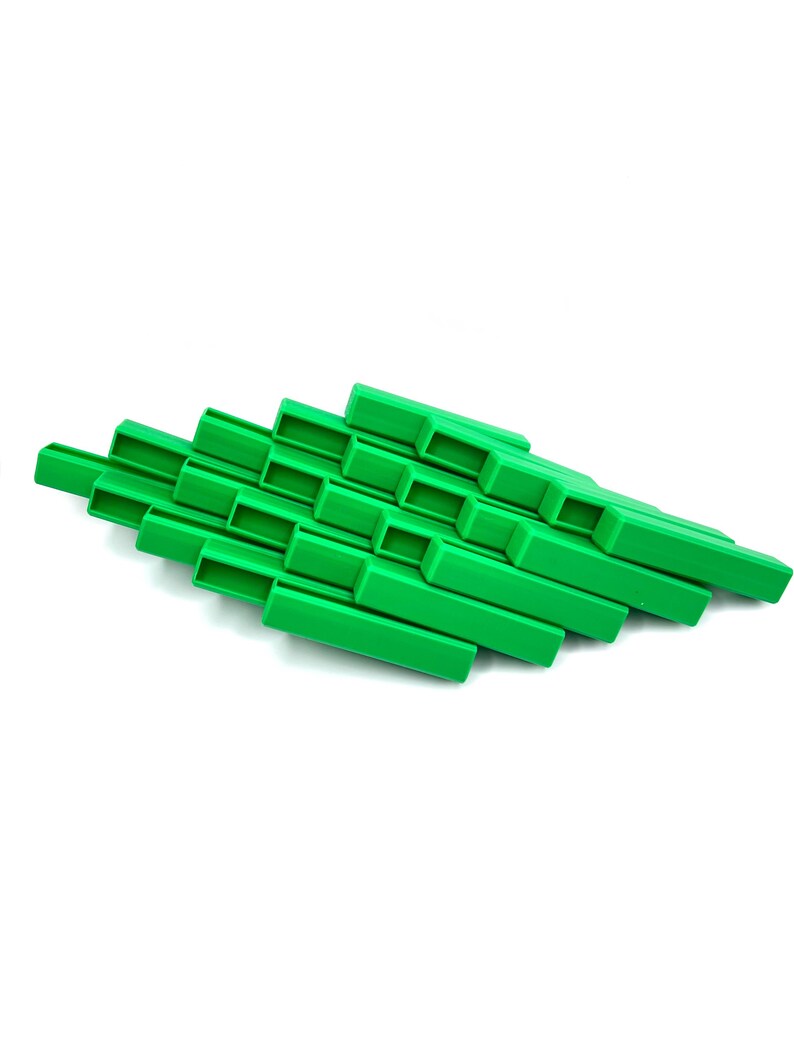 May include: A bright green, geometric, abstract sculpture. The object is composed of rectangular blocks arranged in a layered, diagonal pattern. The blocks have a hollow, open design. The sculpture is set against a white background.