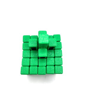 May include: A green cube puzzle composed of smaller green cubes arranged in a three-dimensional structure. The puzzle is set against a white background, highlighting the vibrant green color and geometric design. The cubes are uniform in size and shape.