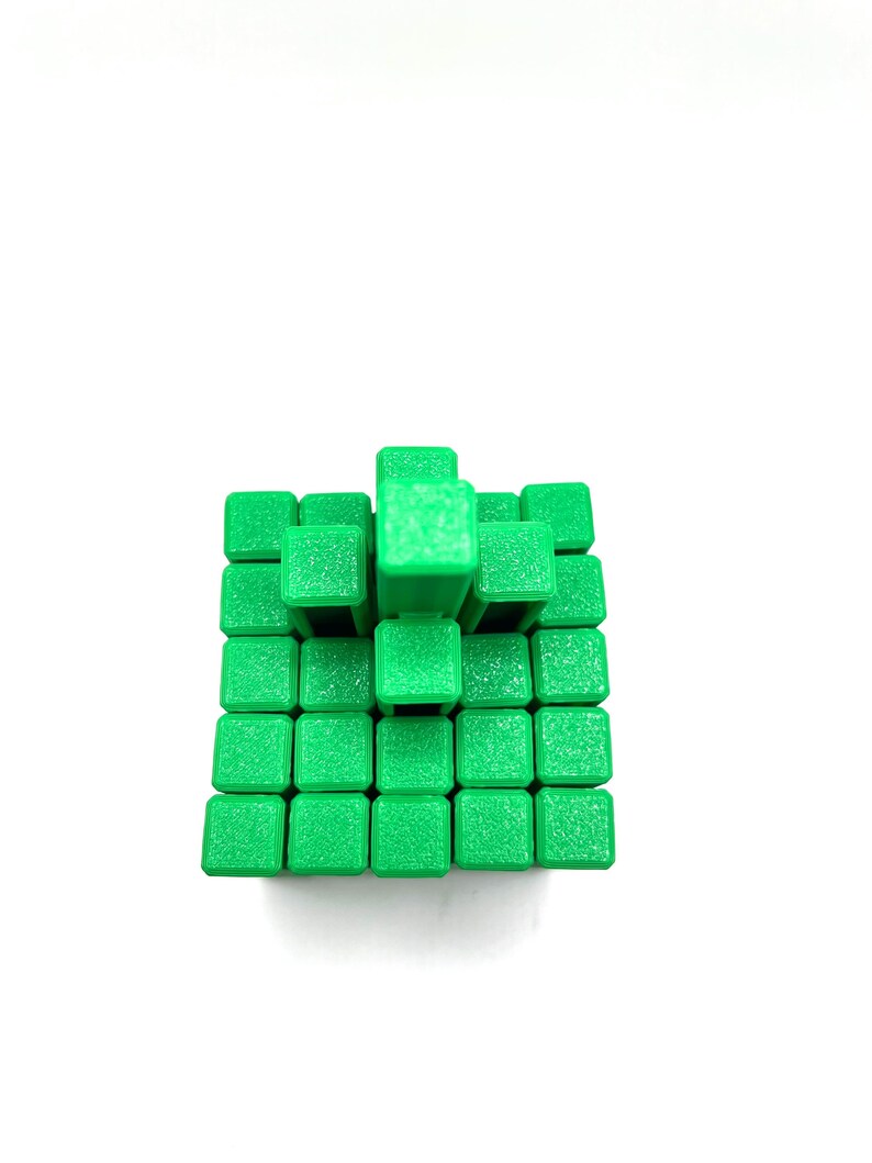 May include: A green cube puzzle composed of smaller green cubes arranged in a three-dimensional structure. The puzzle is set against a white background, highlighting the vibrant green color and geometric design. The cubes are uniform in size and shape.