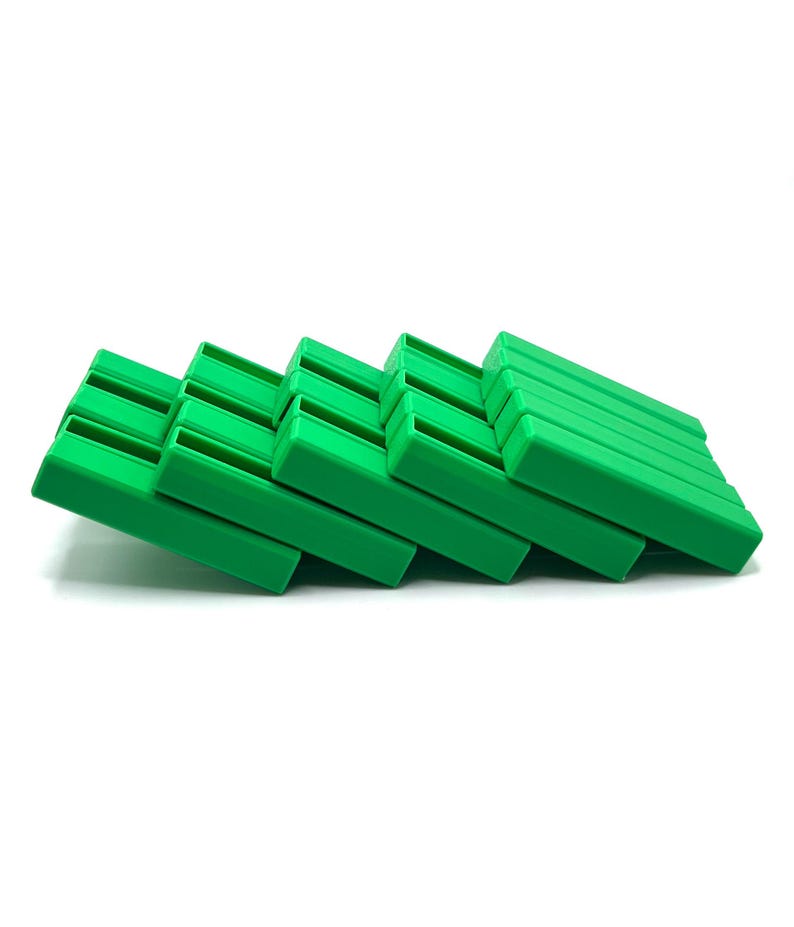 May include: A stack of bright green plastic soap dishes, each with a rectangular shape and a series of parallel ridges on the top surface. The dishes are arranged in a diagonal line against a white background.