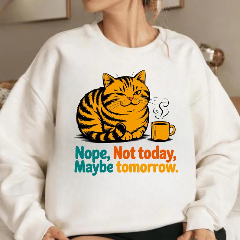 Pode incluir: Camisola branca com um gato de desenho animado com listras laranja e pretas, piscando e sentado ao lado de uma caneca de caf&eacute; amarela. O texto diz: "Nope, Not today, Maybe tomorrow."
