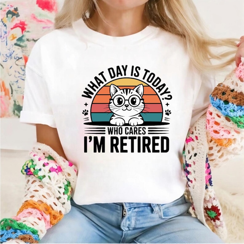 Pode incluir: Camiseta branca com um gr&aacute;fico de um gato usando &oacute;culos, em um design de p&ocirc;r do sol. O texto diz "WHAT DAY IS TODAY? WHO CARES I'M RETIRED". O design inclui pegadas e um esquema de cores retr&ocirc;.