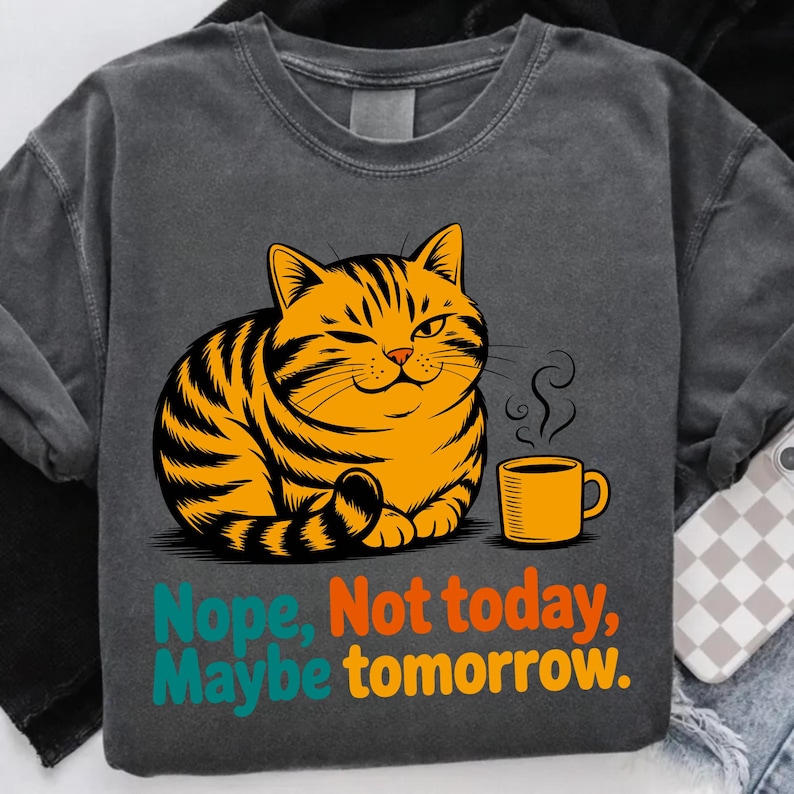 Pode incluir: Camisola cinza escuro com um gato malhado laranja piscando, com listras pretas e uma caneca de caf&eacute; amarela. O texto "Nope, Not today, Maybe tomorrow" &eacute; impresso em turquesa e laranja.