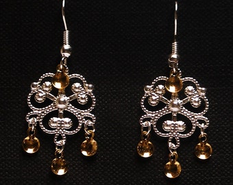 Peut inclure: Une paire de boucles d'oreilles en argent avec un motif filigrané délicat et des accents dorés. Les boucles d'oreilles ont un design de goutte pendante avec plusieurs petites perles dorées.
