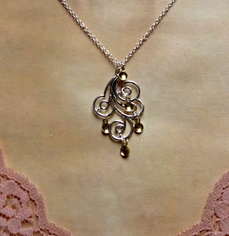 Peut inclure: Un collier en argent avec un pendentif en or pr&eacute;sentant un motif d&eacute;licat et tourbillonnant. Le pendentif comporte plusieurs petites accents ronds en or.
