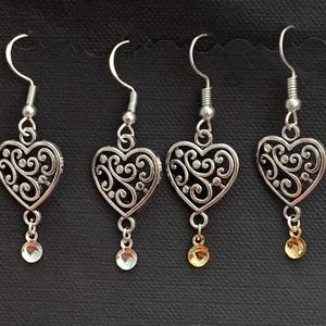 May include: Three pairs of silver heart-shaped dangle earrings with a filigree design. Each earring has a small silver or gold bead at the bottom.