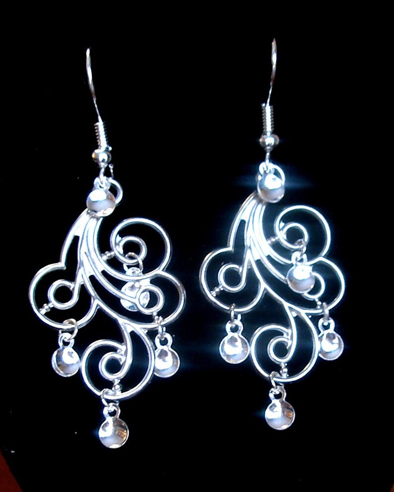 Peut inclure: Une paire de boucles d'oreilles pendantes en argent avec un motif d&eacute;licat et tourbillonnant et de petites perles rondes qui pendent du bas.