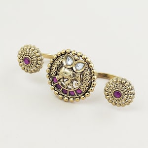 May include: Gold-toned hand jewelry featuring a central circular design with an elephant motif, surrounded by a beaded border and adorned with pink and clear gemstones. Two smaller, matching circular accents with pink stones complete the design.