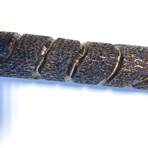 May include: Close-up of a dark brown, textured wooden object with a spiral design. The object has a glossy finish and appears to be a decorative element or part of a larger piece. The wood grain is visible, adding to its rustic appeal.