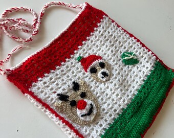 May include: A handmade crochet Christmas bag with a white open weave. The bag features red, green, and white accents, with a reindeer and Santa hat design. The strap is red and white twisted yarn.