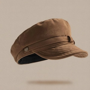 Puede incluir: Gorra de estilo marinero marr&oacute;n con un dise&ntilde;o estructurado. La gorra presenta una visera corta y curvada y una banda con cierre de bot&oacute;n. El sombrero est&aacute; hecho de un material suave y texturizado.