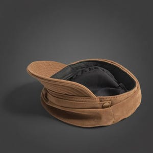 Puede incluir: Gorra newsboy de ante marr&oacute;n con visera curva y detalle de bot&oacute;n. El interior est&aacute; forrado con tela negra. Un sombrero de estilo cl&aacute;sico, adecuado para varios atuendos.