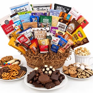 May include: A large woven basket filled with various snack food packages including Fisher's popcorn, Tate's cookies, and Keebler fudge stripes. Three white plates hold assorted cookies, pretzels, and chocolates, with a mug of popcorn nearby.