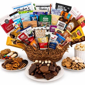 May include: A large woven basket filled with an assortment of packaged snacks, including popcorn, cookies, and chocolate bars. Surrounding the basket are four white plates containing loose cookies, pretzels, chocolates, and a mug of popcorn.