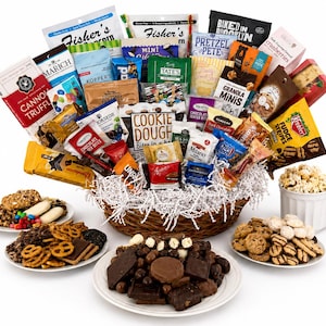 May include: A large woven basket filled with an assortment of packaged snacks, including cookies, popcorn, and chocolate, surrounded by four white plates containing loose cookies, pretzels, chocolates, and a mug filled with popcorn.