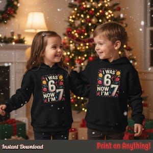 Happy boy and girl wearing matching black hoodies with the “I Was 6 Now I’m 7” design, standing near a Christmas tree with gifts. Shows family or sibling birthday celebration vibes.