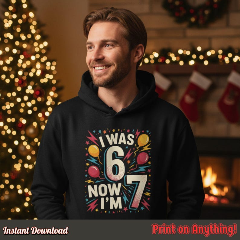 Man in a black hoodie with the “I Was 6 Now I’m 7” print standing by a lit fireplace and Christmas decorations, showing unisex appeal and comfortable fit for family matching outfits.