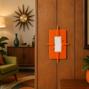 May include: A rectangular orange light switch cover plate featuring a central white rocker switch and four pointed starburst-shaped protrusions extending from the top, bottom, left, and right sides, mounted on a vertical wood-paneled wall surface.