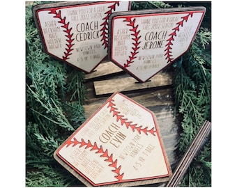 Puede incluir: Tres placas de madera con forma de béisbol con costuras rojas y fondo blanco. Cada placa tiene una inscripción personalizada con el texto "Gracias por una gran temporada de otoño 2022" y el nombre de un entrenador. Las placas están en un soporte de madera.
