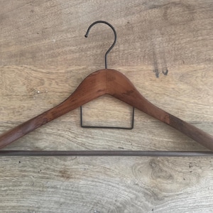 May include: A wooden clothes hanger with a smooth, dark brown finish. It features a curved top bar, a black metal hook at the center, a rectangular black metal wire support below the hook, and a horizontal black metal bar across the bottom.