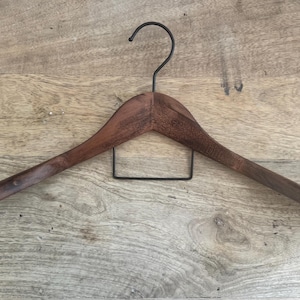 May include: A dark brown wooden clothes hanger featuring a curved shoulder design and a black metal hook at the top. A rectangular black metal bar is attached horizontally beneath the wooden frame to provide additional support for garments.