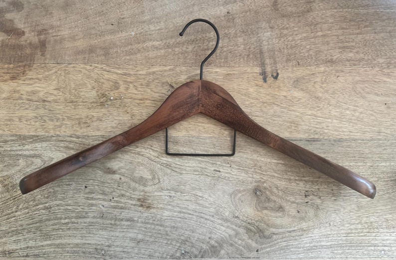 May include: A dark brown wooden clothes hanger featuring a curved shoulder design and a black metal hook at the top. A rectangular black metal bar is attached horizontally beneath the wooden frame to provide additional support for garments.
