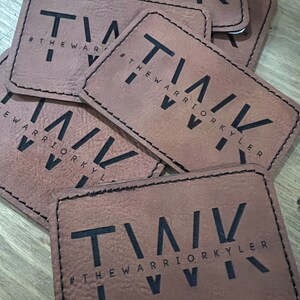 May include: Close-up of several brown leather patches with black stitching. Each patch features the text "T/AV #THEWARRIORKYLER" in a bold, stylized font.