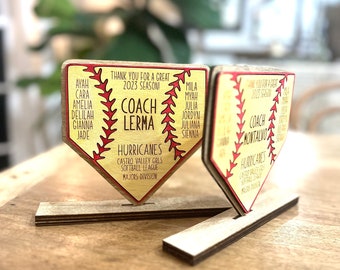 Puede incluir: Dos placas de madera con forma de base de béisbol con costuras rojas y texto. Una placa dice "Coach Lerma" y "Hurricanes" con los nombres de los jugadores. La otra placa dice "Coach Montalvo" y "Hurricanes" con los nombres de los jugadores.