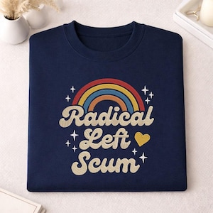 May include: A navy blue sweatshirt featuring a rainbow design and the words "Radical Left Scum". The graphic includes a rainbow, stars, and a yellow heart. The sweatshirt is neatly folded.