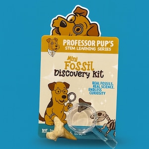 Puede incluir: Un Mini Kit de Descubrimiento de Fósiles con un personaje de perro de dibujos animados. El kit incluye un fósil, una lupa y el texto "Professor Pup's STEM Learning Series". El kit promete "Real Fossils, Real Science, Endless Curiosity".