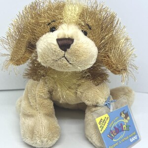 Puede incluir: Un perro de peluche con pelaje color canela, orejas largas y peludas de color marrón y una nariz marrón oscuro. En su pata lleva una etiqueta de plástico transparente con el texto Webkinz, Adopt a pet, discover a virtual world, Open tag at home.