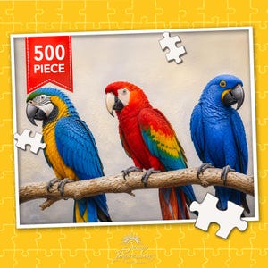 May include: A 500 piece jigsaw puzzle featuring three parrots perched on a branch. The left parrot is blue and yellow, the center parrot is red, yellow, and green, and the right parrot is solid blue. A red banner in the top left corner reads 500 PIECE.