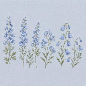 May include: Embroidered floral design featuring various blue flowers, including delphiniums and bellflowers, with green stems and leaves. The flowers are intricately stitched on a light blue fabric, creating a delicate and detailed botanical illustration.