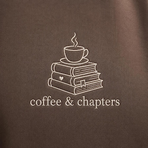May include: Brown sweatshirt with a white embroidered design. The design features a stack of books with a coffee cup on top, and the words "coffee & chapters" below.