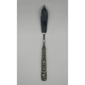 May include: Silver butter knife with a curved blade. The handle is intricately decorated with a floral pattern. The knife is designed for spreading butter or other soft spreads. The knife is made of a shiny, reflective metal.