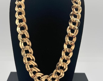 May include: A gold-colored chain necklace with large, interlocking links. The necklace is displayed on a black velvet bust, showcasing its bold design and polished finish. The jewelry piece is a statement accessory.