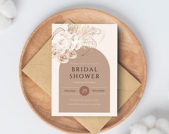 May include: A bridal shower invitation card with floral and arch design, set on a wooden plate with a kraft paper envelope. The invitation features the text "BRIDAL SHOWER" and event details.
