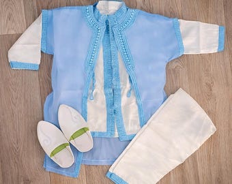 May include: A light blue and white outfit with matching white slippers. The outfit includes a jacket with blue trim, a white shirt, and white trousers with blue trim. The slippers are white with green insoles.