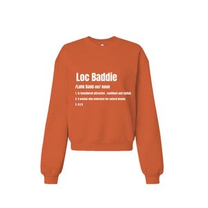 May include: An orange crewneck sweatshirt with the text "Loc Baddie" in white. The text is followed by a definition that includes the words "attractive, confident, and stylish."