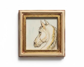 May include: A framed watercolor painting of a horse's head in profile. The artwork features a cream-colored horse with a detailed mane and eye, set against a pale blue background. The frame is a square shape with a gold inner border and a cream-colored outer frame.