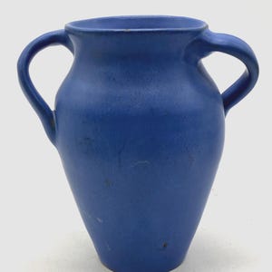 May include: A deep blue ceramic vase with two loop handles. The vase has a bulbous body and a wide mouth. The surface has a slightly textured finish. The vase is a classic shape.