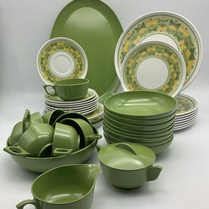 Op de afbeelding: Een complete vintage groen en wit servies set. De set bevat borden, kommen, kopjes, schotels, een serveerschaal en serveerschalen. De borden en schotels hebben een geel en groen geometrisch patroon.