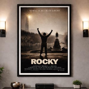 May include: A framed "Rocky" movie poster on a grey wall. The poster shows a silhouette of a man with arms raised, the title "Rocky," and the tagline "His Whole Life Was A Million-to-One Shot."