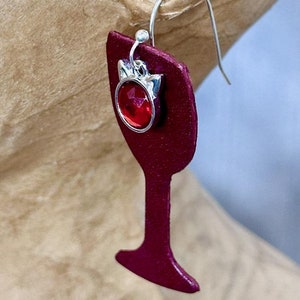 May include: Burgundy red leather earrings shaped like a wine glass with a red rhinestone charm.