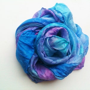 May include: A hand-dyed silk scarf in shades of blue and purple, artfully arranged. The fabric is soft and flowing, with a watercolor effect. The scarf is a beautiful accessory.