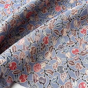 May include: Close-up of a fabric with a repeating floral pattern. The design features stylized leaves, berries, and flowers in shades of red, brown, and purple against a light blue background. The fabric is folded, revealing a white edge.