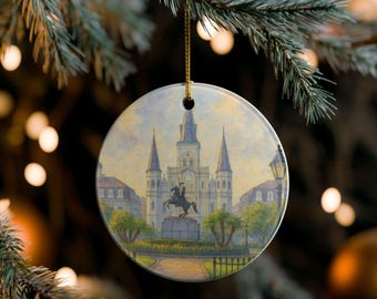Puede incluir: Adorno navideño redondo con una pintura de acuarela de una catedral con agujas, una estatua y edificios circundantes. El adorno cuelga de un hilo dorado sobre un fondo borroso de luces navideñas y una rama de pino.