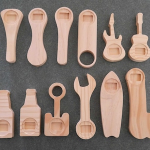 May include: A collection of wooden bottle openers in various shapes, including guitars, surfboards, and wrenches. The openers are made of light-colored wood and are arranged on a gray surface.
